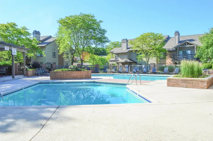 Sunny residential complex with inviting swimming pools, lush greenery, and charming brick-lined landscaping.