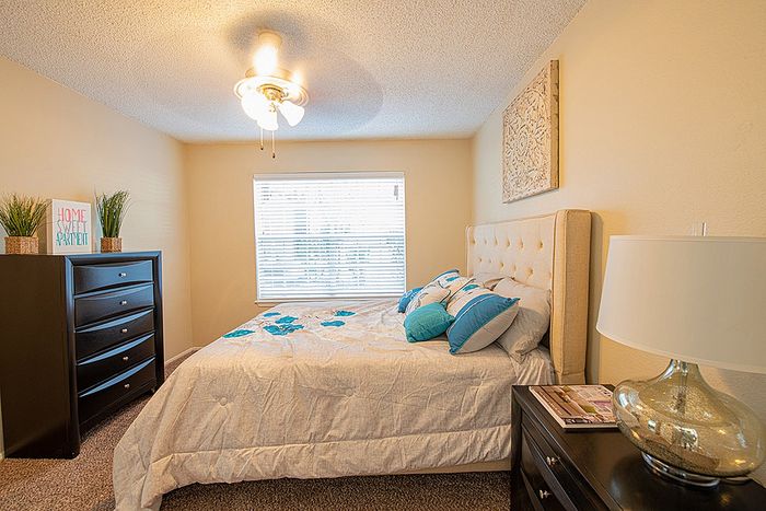 Cozy bedroom featuring a plush bed with blue accent pillows, elegant lamps, and natural light through a large window, creating a warm and inviting atmosphere.