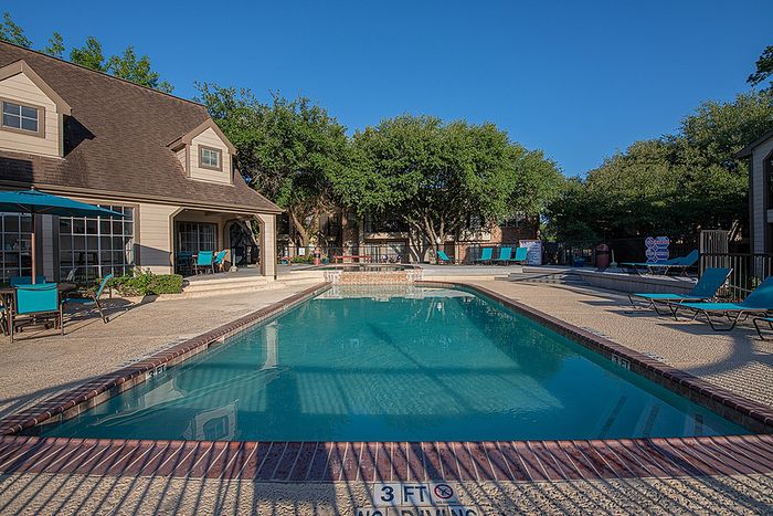 Charming apartment complex featuring a sparkling pool with relaxing lounge chairs and lush green surroundings.