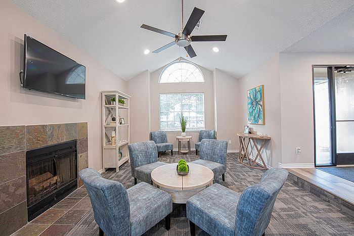 Bright and inviting living space featuring a cozy fireplace, modern blue chairs, and abundant natural light through large windows.