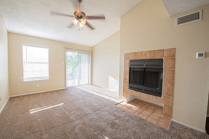 Bright living room with plush carpet, a cozy tiled fireplace, and large windows offering ample natural light.