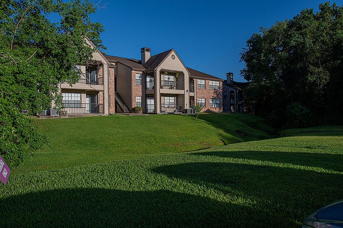 Charming apartment complex with classic brick facade surrounded by lush greenery and vibrant blue skies.
