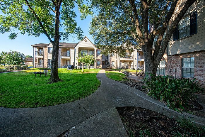 Charming apartment complex with lush greenery and shaded pathways creating a serene living environment.