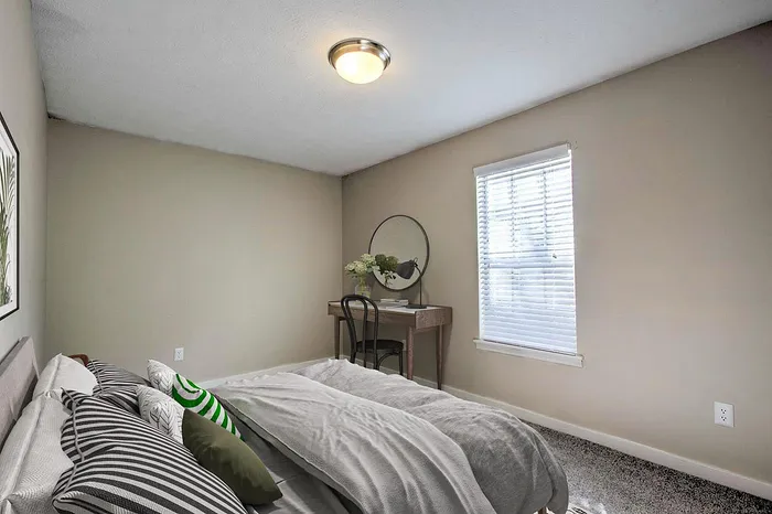 Inviting bedroom with cozy bedding, stylish dressing table, and bright natural light from a large window.