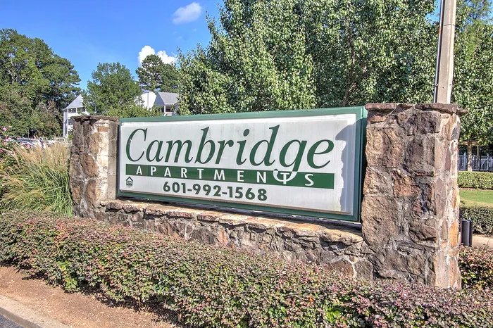Welcoming entrance sign for Cambridge Apartments surrounded by lush greenery and vibrant landscaping.