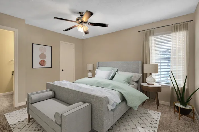 Inviting bedroom with modern decor, featuring a plush gray bed, cozy lighting, and a refreshing potted plant next to a large window.