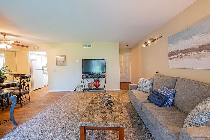 Cozy living room featuring elegant decor with a plush sofa, stylish coffee table, and wall-mounted TV, complemented by a dining area with modern seating, under warm, inviting lighting.