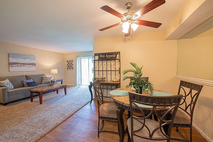 Cozy living and dining area with elegant ceiling fan, featuring a comfortable sofa, rustic coffee table, chic dining set, and stylish decor in a warm, inviting atmosphere.