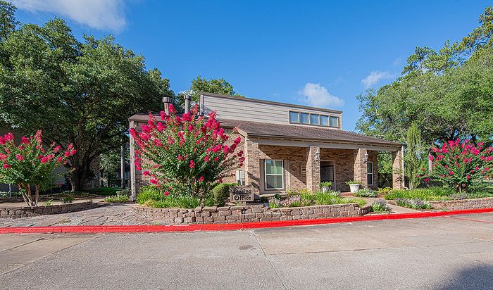 Charming leasing office surrounded by vibrant flowering plants and lush trees, set against a clear blue sky.