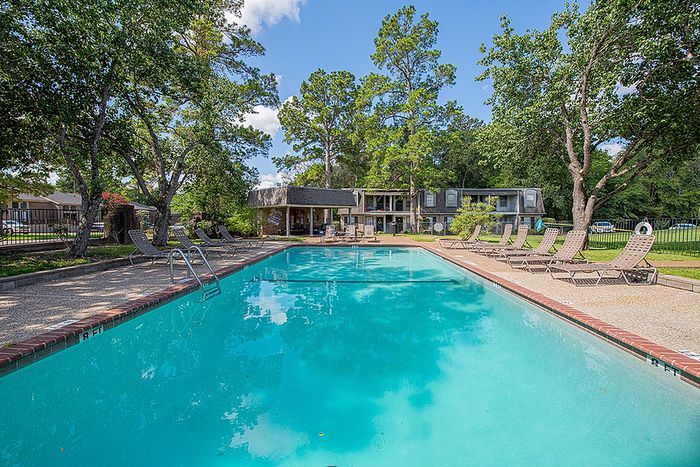 Inviting outdoor pool surrounded by lush trees and sun loungers, enhancing a serene residential setting.