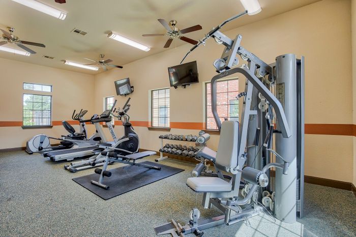 Modern apartment gym equipped with cardio machines, weight stations, and flat-screen TVs, offering a bright and inviting workout space.