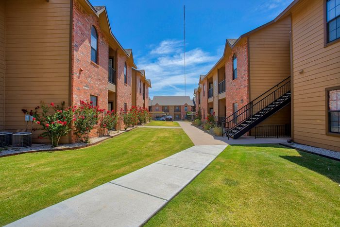 Inviting apartment complex with charming brick exteriors, manicured lawns, and vibrant rose bushes under a bright blue sky.