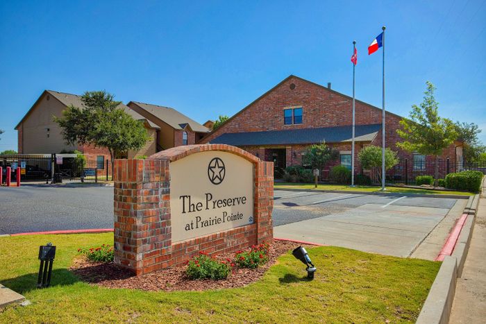 Charming entrance to The Preserve at Prairie Pointe with brick signage, vibrant landscaping, and clear blue skies.