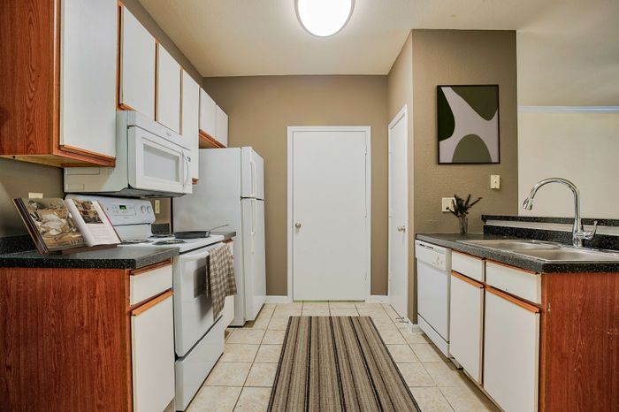 Modern kitchen with sleek countertops, white appliances, and warm wooden cabinetry, ideal for culinary creativity.