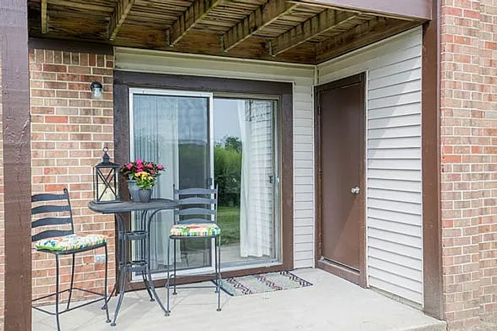 Charming patio with cozy seating, vibrant flowers, and elegant sliding glass doors leading to a serene garden view.