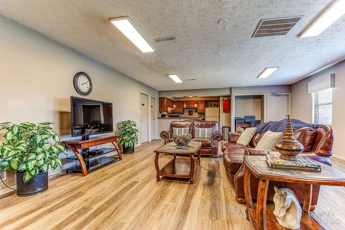 Inviting open-concept living room with cozy leather sofas, wooden flooring, large TV, and elegant decor, leading into a warm and functional kitchen space.