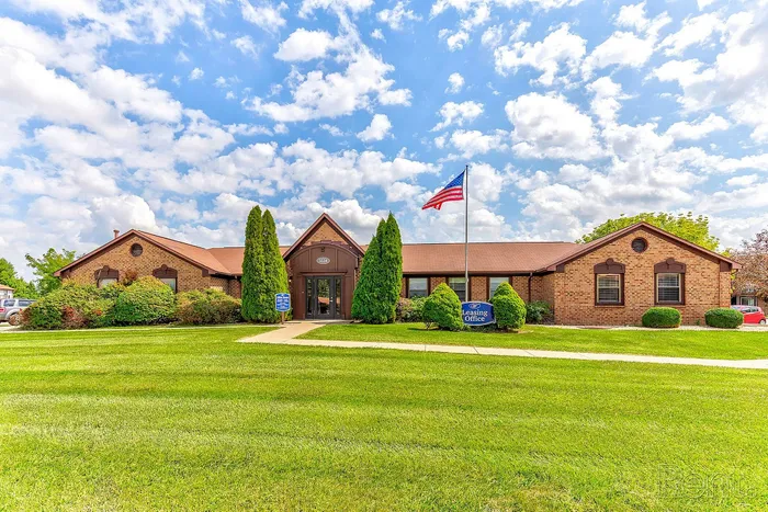 Charming leasing office with brick facade, lush green lawn, and an American flag under a bright blue sky.