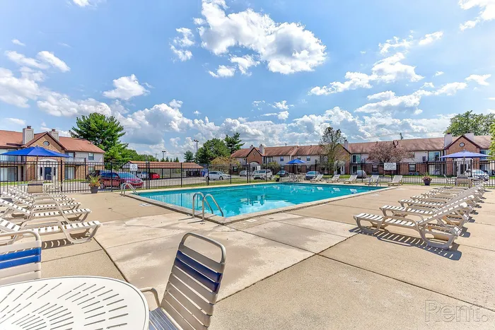Inviting community swimming pool with sun loungers, nestled in a charming residential area under a bright blue sky.