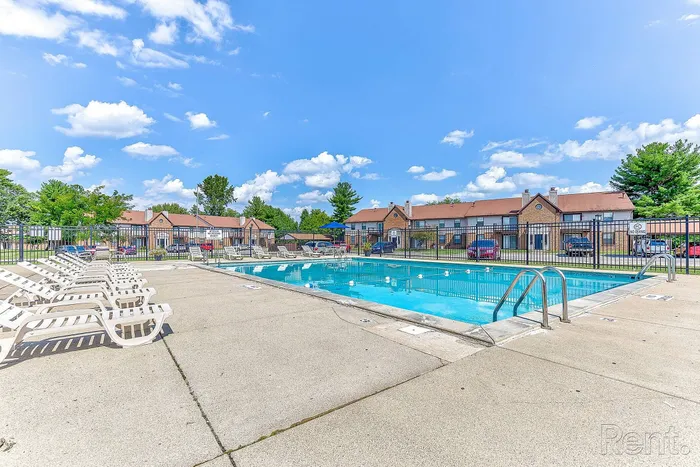 Vibrant community pool area with inviting lounge chairs under a clear blue sky, perfect for relaxation and leisure.