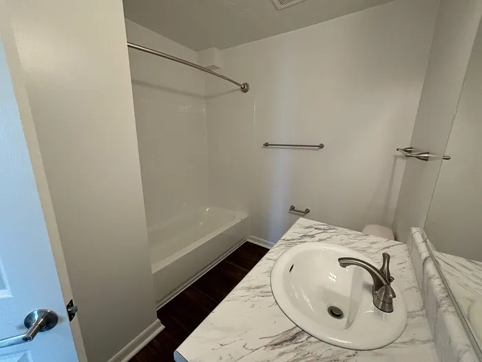 Modern bathroom with elegant white marble countertop, stylish stainless steel fixtures, and a serene bathtub shower combo.