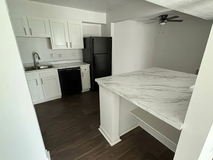 Modern kitchen with elegant white cabinetry, sleek black appliances, and a stylish marble countertop island on rich hardwood flooring.