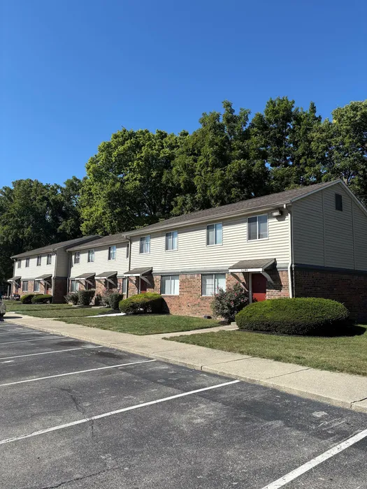 Charming row of townhouses with beautifully manicured greenery and ample parking on a sunny day.