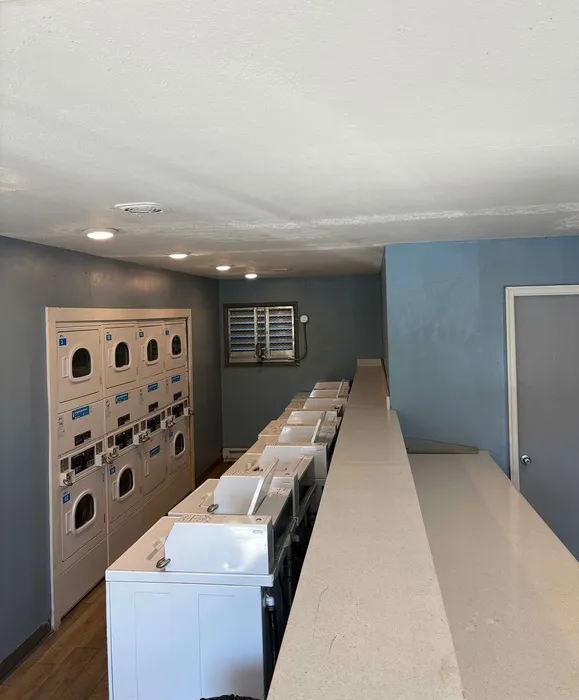 Modern laundry room with multiple stacked washers and dryers, featuring sleek countertops and ample lighting.