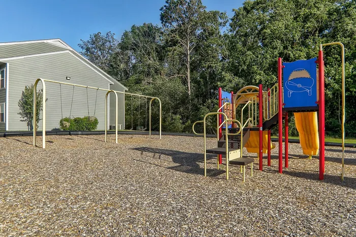 Inviting playground with swings and colorful slide nestled amidst lush greenery, perfect for family fun.