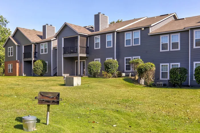 Charming apartment complex with modern architecture, lush green lawn, and a cozy outdoor grill area.