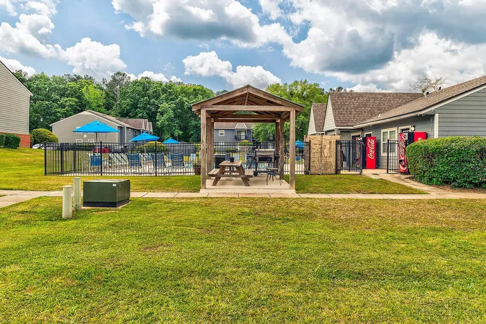 Charming outdoor picnic area beside a pool with vibrant blue umbrellas and lush greenery, perfect for relaxation and leisure.