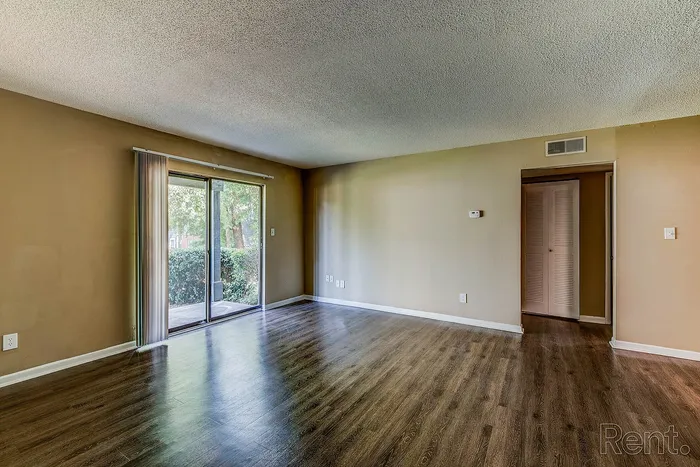 Bright and airy living room with chic wood flooring, sliding glass doors opening to lush greenery, and neutral wall tones ready for your personal touch.