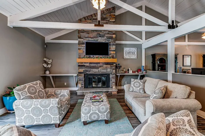 Inviting living room with vaulted ceiling, stone fireplace, and stylish patterned furniture. Cozy seating area surrounded by rustic decor and natural lighting.