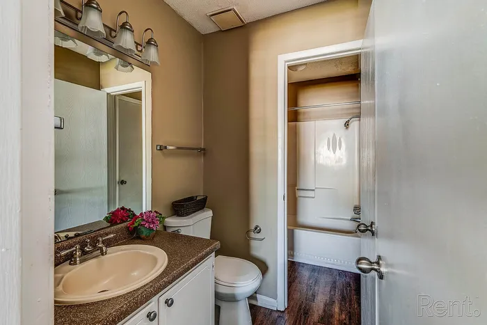 Elegant bathroom with stylish lighting, a modern sink, and vibrant floral accents, leading to a spacious shower area with sleek wood flooring.