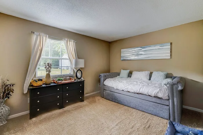 Cozy bedroom with stylish gray daybed, elegant dresser, and large window offering natural light.