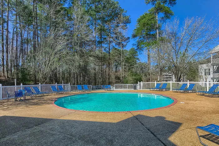 Tranquil outdoor pool area surrounded by lush trees, featuring comfortable lounge chairs and a serene atmosphere.