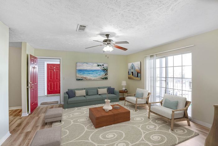 Inviting living room with modern decor, featuring a cozy gray sofa, patterned area rug, and elegant artwork. Bright natural light streams through large glass doors, highlighting the stylish design.