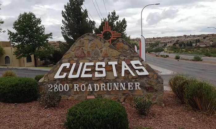 Inviting stone entrance sign reading 'Cuestas 2800 Roadrunner' surrounded by lush greenery and a scenic suburban backdrop.