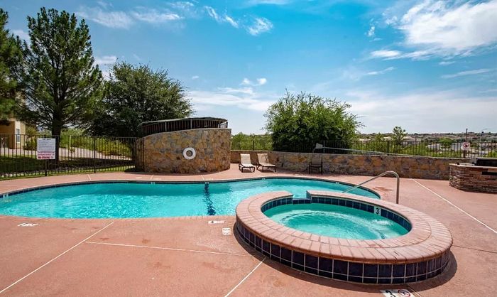 Inviting outdoor pool area with a luxurious hot tub surrounded by scenic greenery, perfect for relaxation under sunny skies.