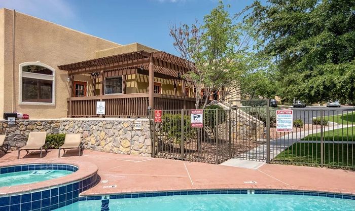 Inviting poolside area with sun loungers in front of a charming stone and wood clubhouse, surrounded by lush greenery.