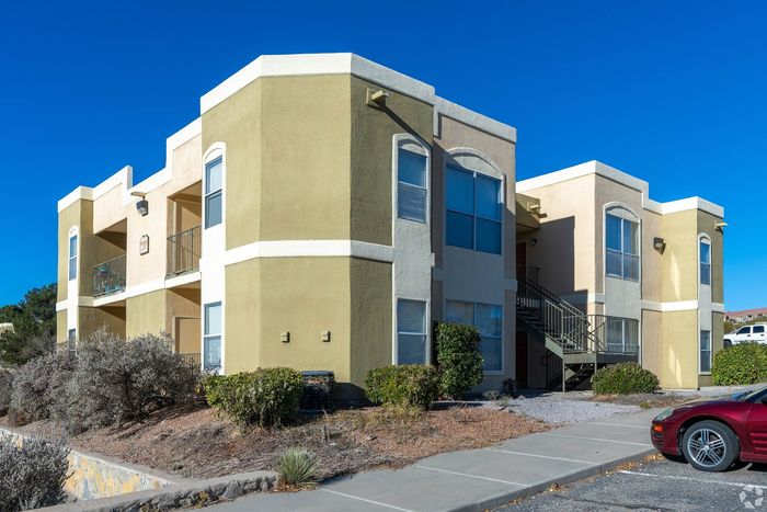 Charming two-story apartment building with stylish architectural design, featuring spacious balconies and surrounded by lush greenery under a clear blue sky.