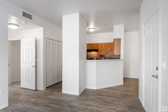 Inviting apartment interior showcasing a modern kitchen with sleek wooden cabinets, adjacent to an open living space with elegant flooring and natural light.