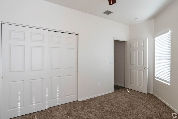 Bright and cozy bedroom featuring plush carpet flooring, ample closet space with sliding doors, and abundant natural light through wide windows.