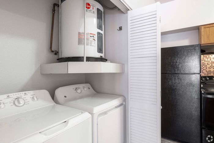 Convenient laundry area with modern washer and dryer, adjacent to a sleek kitchen with black appliances.