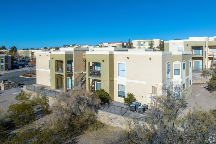 Charming apartment complex with stylish architecture, featuring balconies and lush surroundings under a clear blue sky.