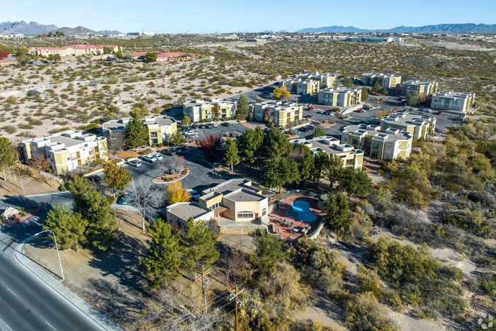 Scenic aerial view of modern apartment complex nestled in a serene landscape with a pool and lush greenery, perfect for tranquil living.