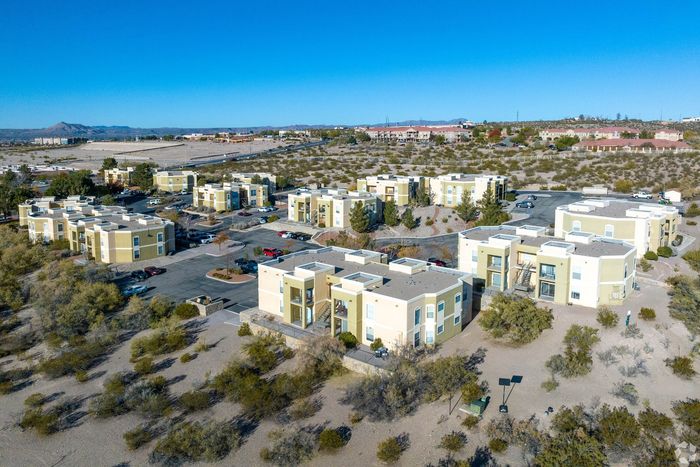 Scenic aerial view of modern desert apartment complex with pastel-colored buildings, ample parking, and vast open spaces.