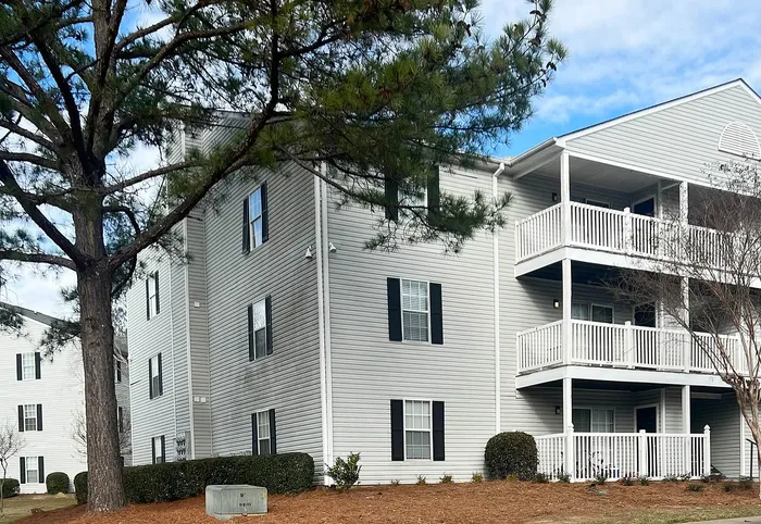Charming apartment building with modern design, featuring spacious balconies and surrounded by lush greenery.