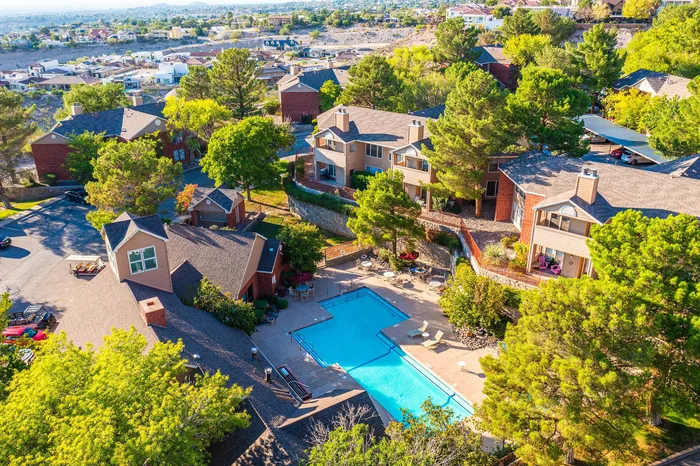 Scenic aerial view of a luxurious apartment complex surrounded by lush greenery, featuring a sparkling pool and beautifully landscaped grounds.