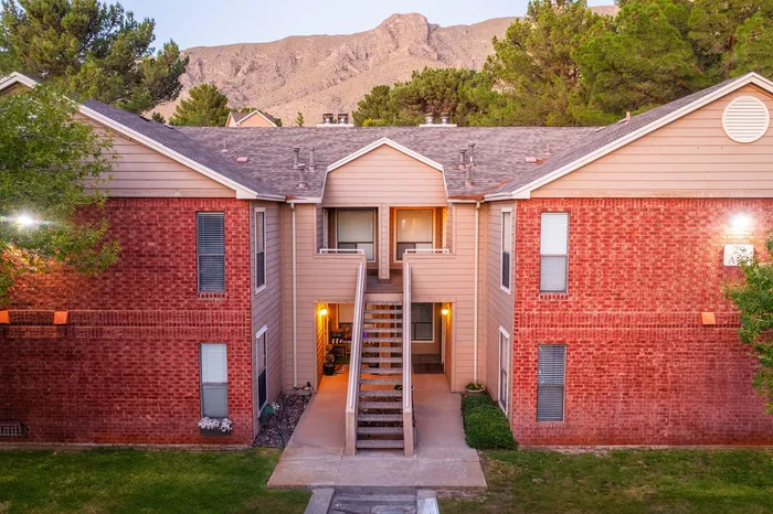 Charming two-story brick apartment complex with inviting balconies, surrounded by lush trees and picturesque mountain views.