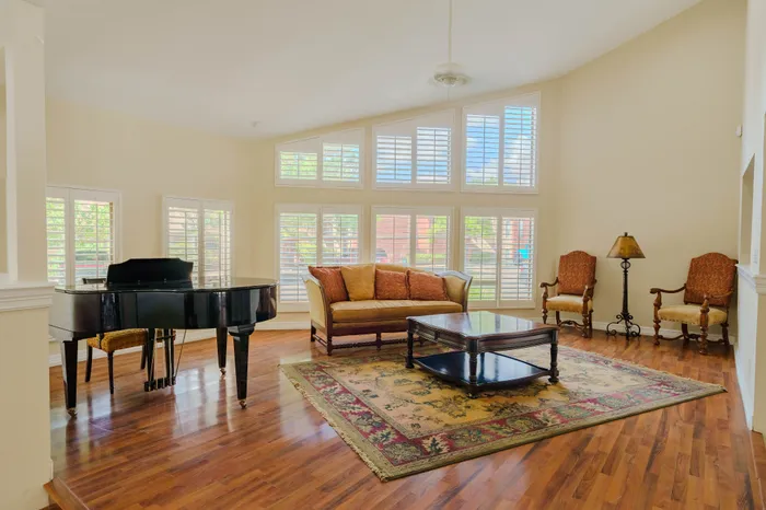 Elegant living room with a grand piano, abundant natural light, and tasteful décor featuring a plush sofa, stylish chairs, and a classic area rug.
